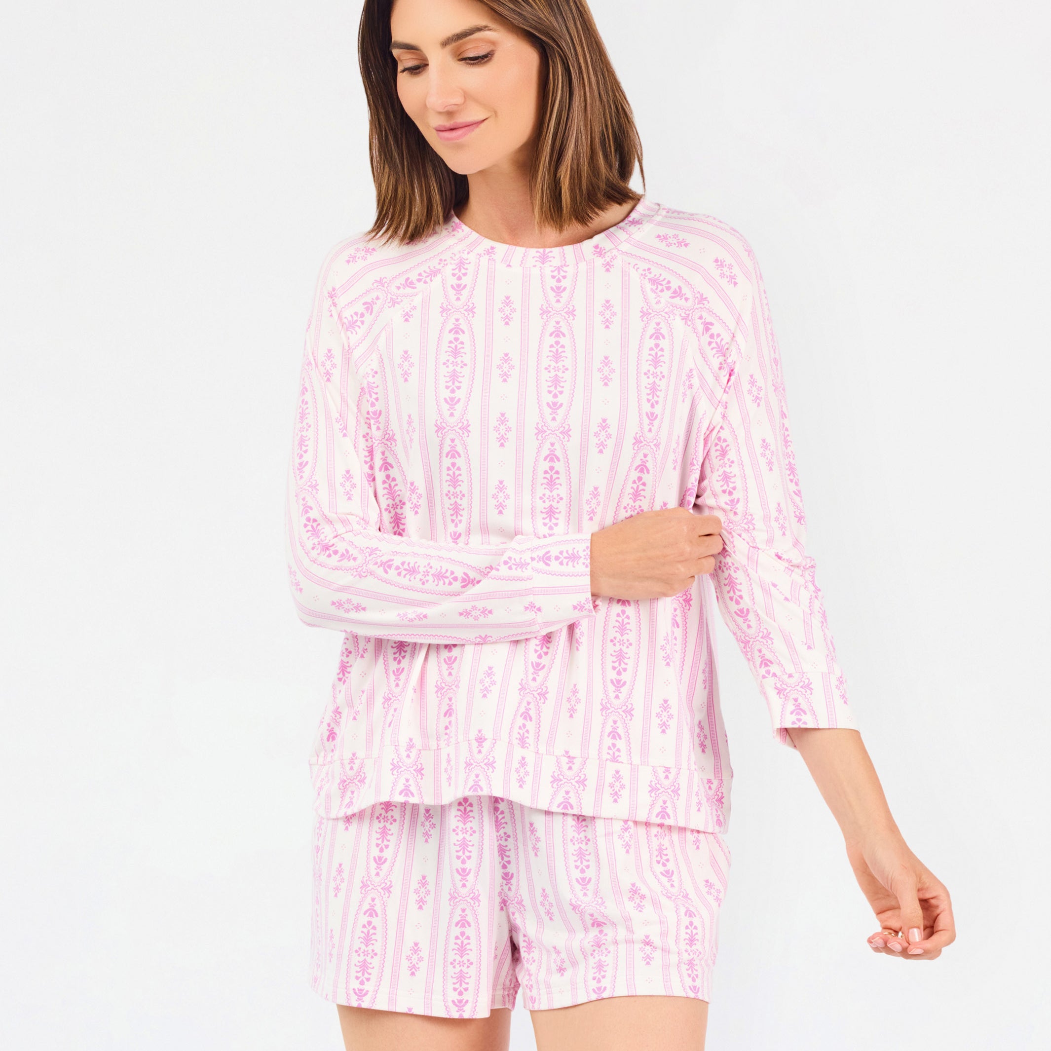 Short brown haired woman wearing a pink/purple floral pajama set on a white background