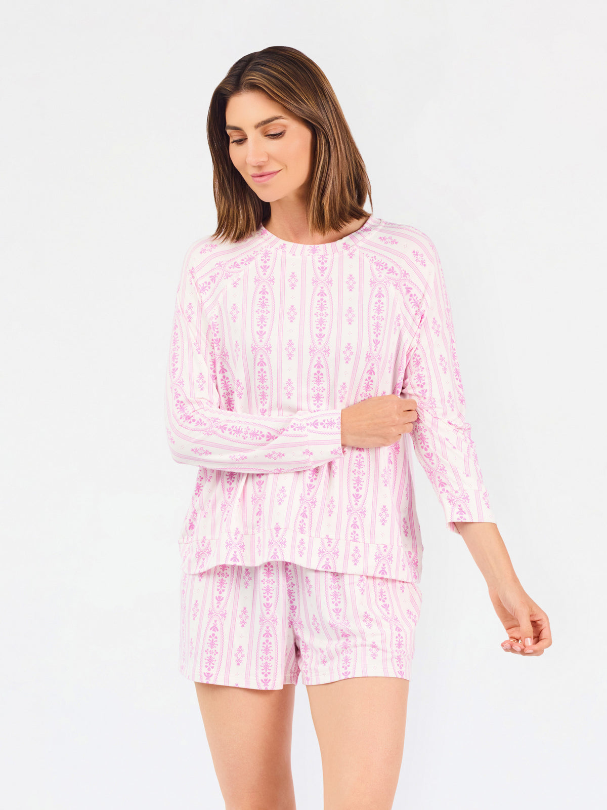 Short brown haired woman wearing a pink/purple floral pajama set on a white background