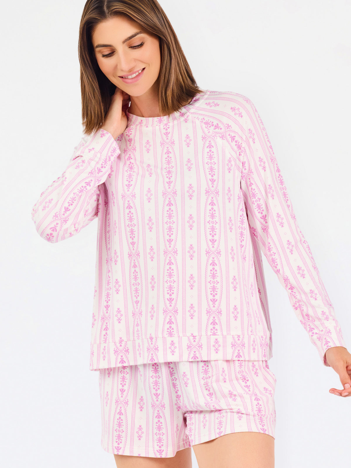 Short brown haired woman wearing a pink/purple floral pajama set on a white background