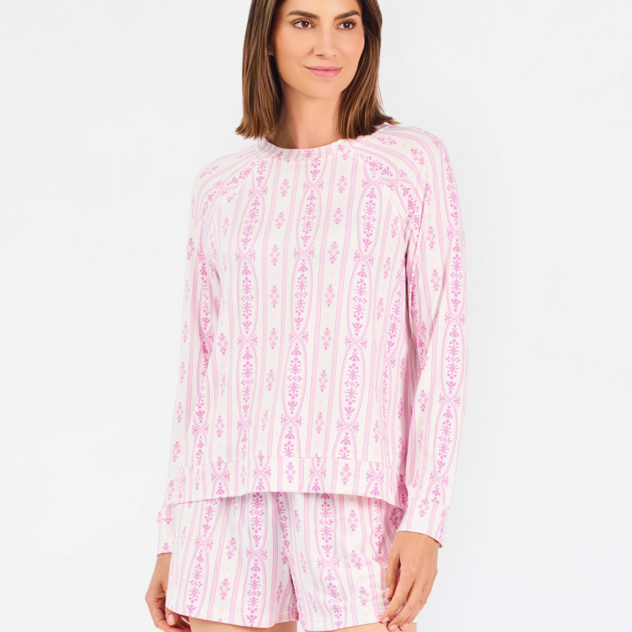 Short brown haired woman wearing a pink/purple floral pajama set on a white background