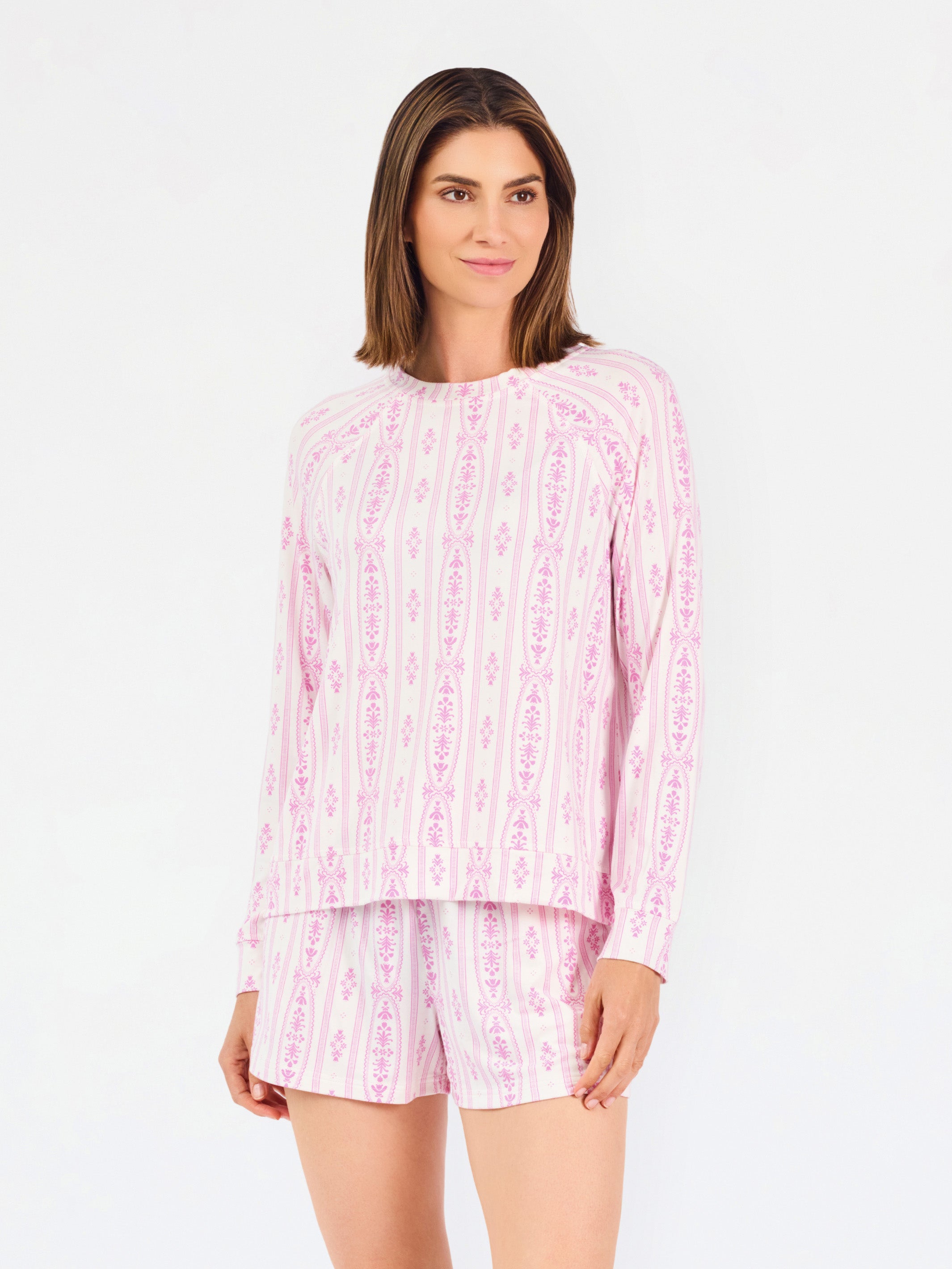 Short brown haired woman wearing a pink/purple floral pajama set on a white background