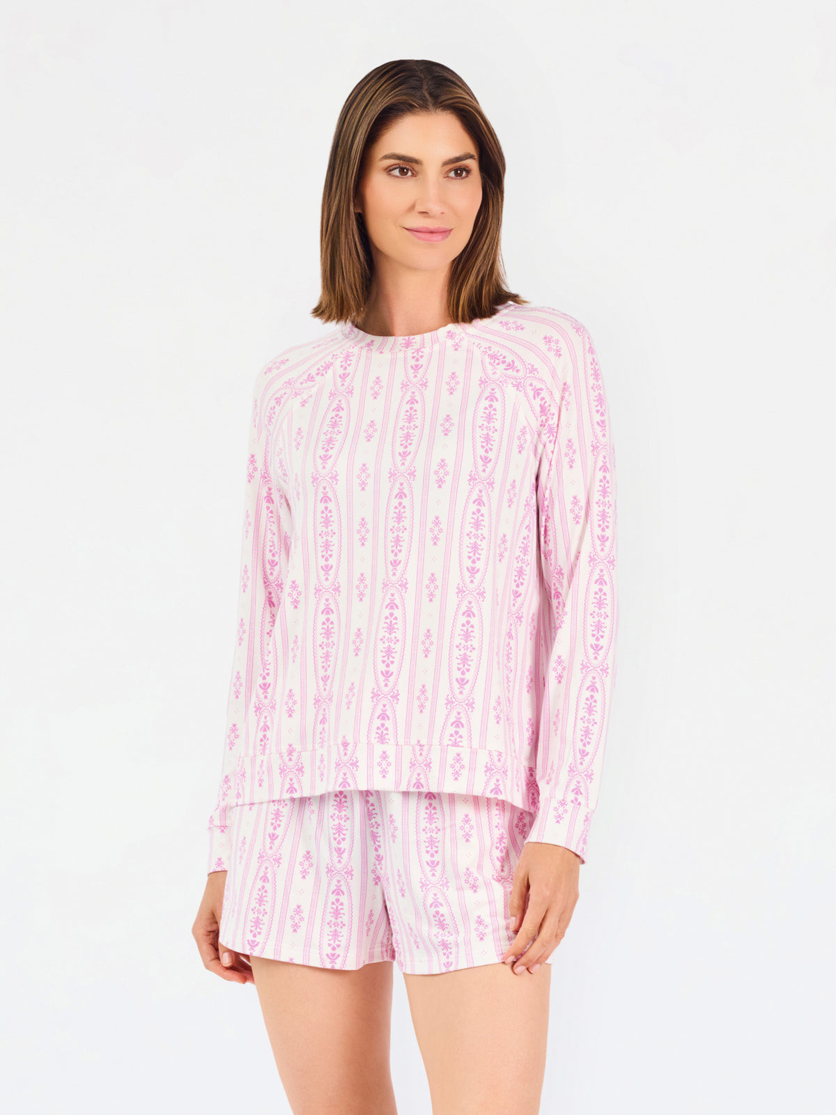 Short brown haired woman wearing a pink/purple floral pajama set on a white background