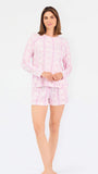 Short brown haired woman wearing a pink/purple floral pajama set on a white background