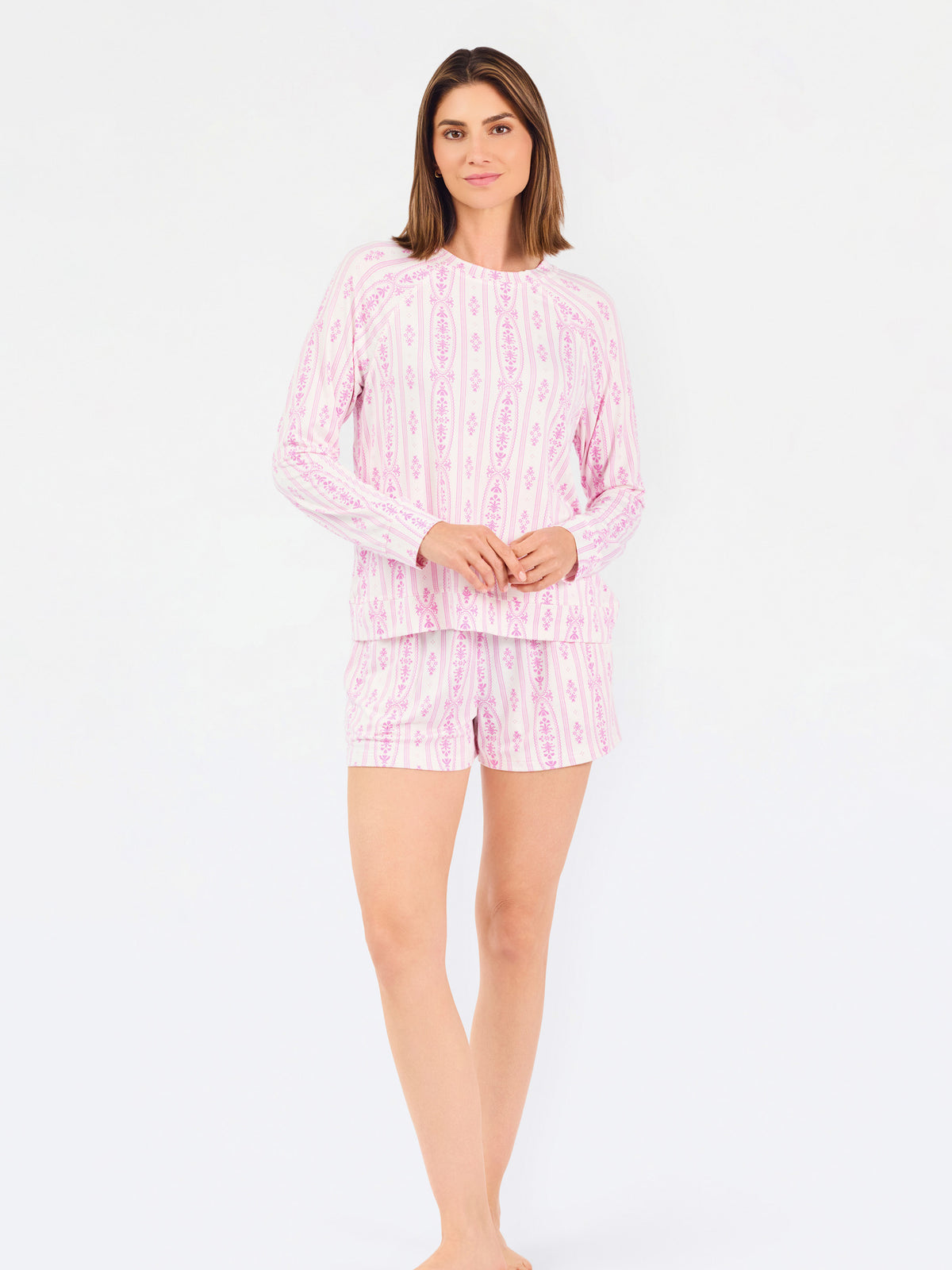 Short brown haired woman wearing a pink/purple floral pajama set on a white background