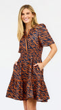 A woman modeling a short-sleeve tiered dress with an orange and navy tiger stripe pattern, standing against a plain white background.