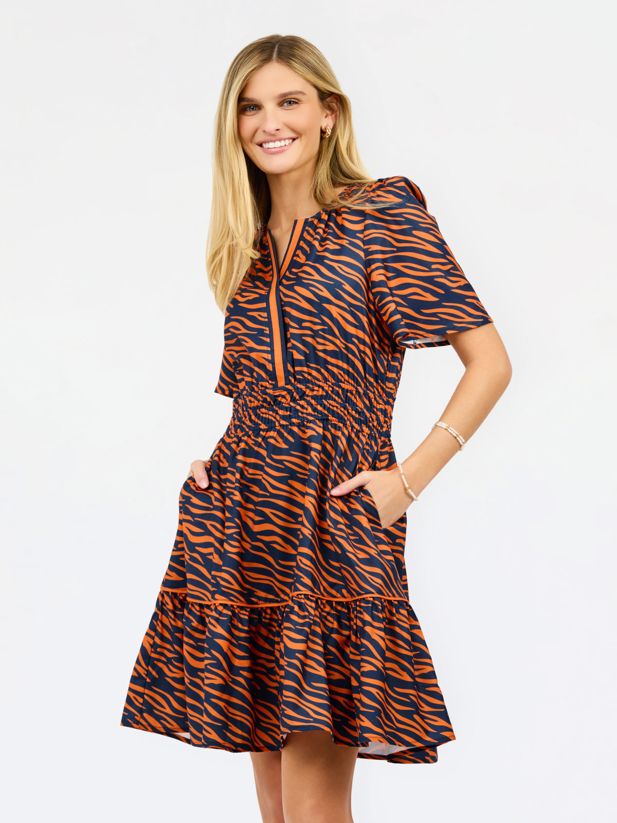 A woman modeling a short-sleeve tiered dress with an orange and navy tiger stripe pattern, standing against a plain white background.