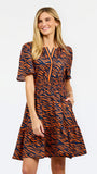 A woman modeling a short-sleeve tiered dress with an orange and navy tiger stripe pattern, featuring a split neckline with orange piping details, set against a plain white studio background.