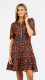 A woman modeling a short-sleeve tiered dress with an orange and navy tiger stripe pattern, featuring a split neckline with orange piping.