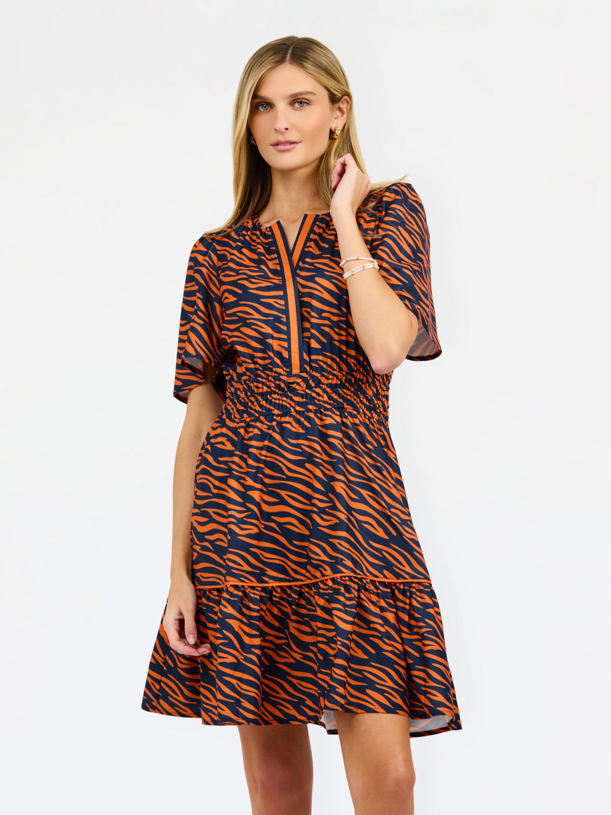 A woman modeling a short-sleeve tiered dress with an orange and navy tiger stripe pattern, featuring a split neckline with orange piping.