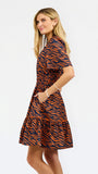 A woman modeling a short-sleeve mini dress with a bold orange and navy tiger stripe pattern, shown from a side-back angle against a plain white studio background.