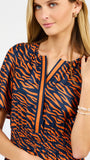 A woman wearing a short-sleeve top with an orange and navy blue tiger stripe pattern, featuring a split V-neckline with orange trim.