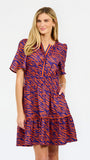 A woman modeling a short-sleeve tiered dress with a purple and orange tiger-like pattern, featuring a split neckline with orange trim and side pockets, set against a plain white background.