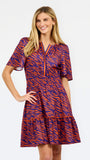 A woman modeling a short-sleeve tiered dress with a purple and orange tiger-like pattern, featuring a split neckline with orange trim and side pockets, set against a plain white background.