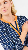 A woman modeling a navy blue and white gingham tiered dress with orange trim details on the neckline and hem, set against a plain light gray background.