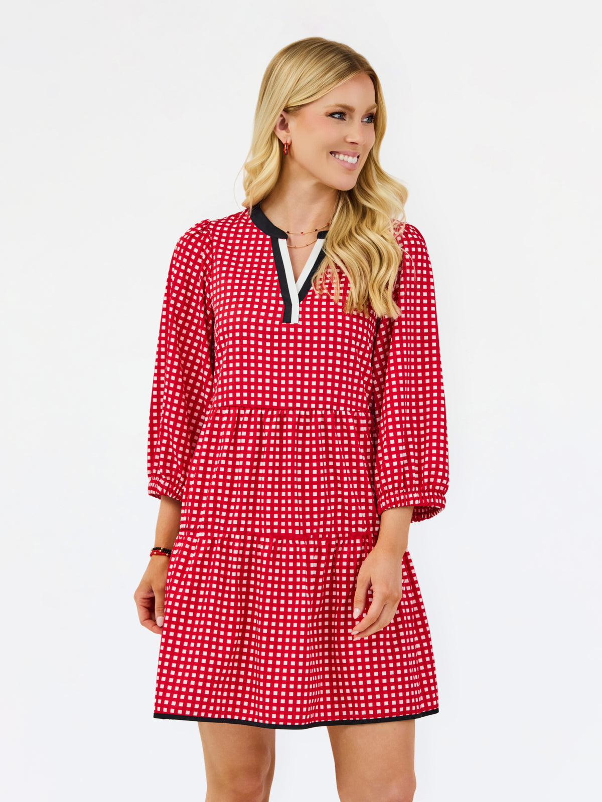 A woman modeling a red and white gingham tiered dress with a black and white split neckline, photographed against a plain white studio background.