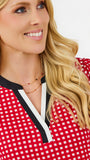 A close-up of a smiling blonde woman wearing a red and white gingham top with a black and white V-neck trim.