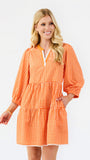 A woman modeling a tiered orange and white gingham mini dress with three-quarter sleeves and a split neckline, set against a plain white studio background.