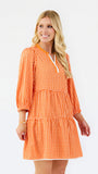 A woman modeling a tiered orange and white gingham mini dress with three-quarter sleeves and a split neckline, set against a plain white studio background.