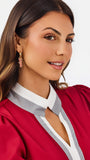 A woman modeling a short-sleeve blouse with puff sleeves, featuring a white collar and keyhole placket with red trim, paired with white pants against a light gray studio background.