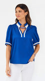 A woman modeling a royal blue short-sleeve blouse with white trim on the collar and cuffs, paired with white pants, against a plain white studio background.