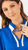 A woman modeling a royal blue short-sleeve blouse with white trim on the collar and cuffs, paired with white pants, against a plain white studio background.