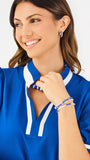A woman modeling a royal blue short-sleeve blouse with white trim on the collar and cuffs, paired with white pants, against a plain white studio background.