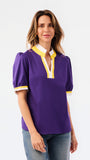 A woman modeling a purple short-sleeve blouse with a white and yellow V-neck collar and yellow striped cuffs, paired with blue jeans, against a plain white background.