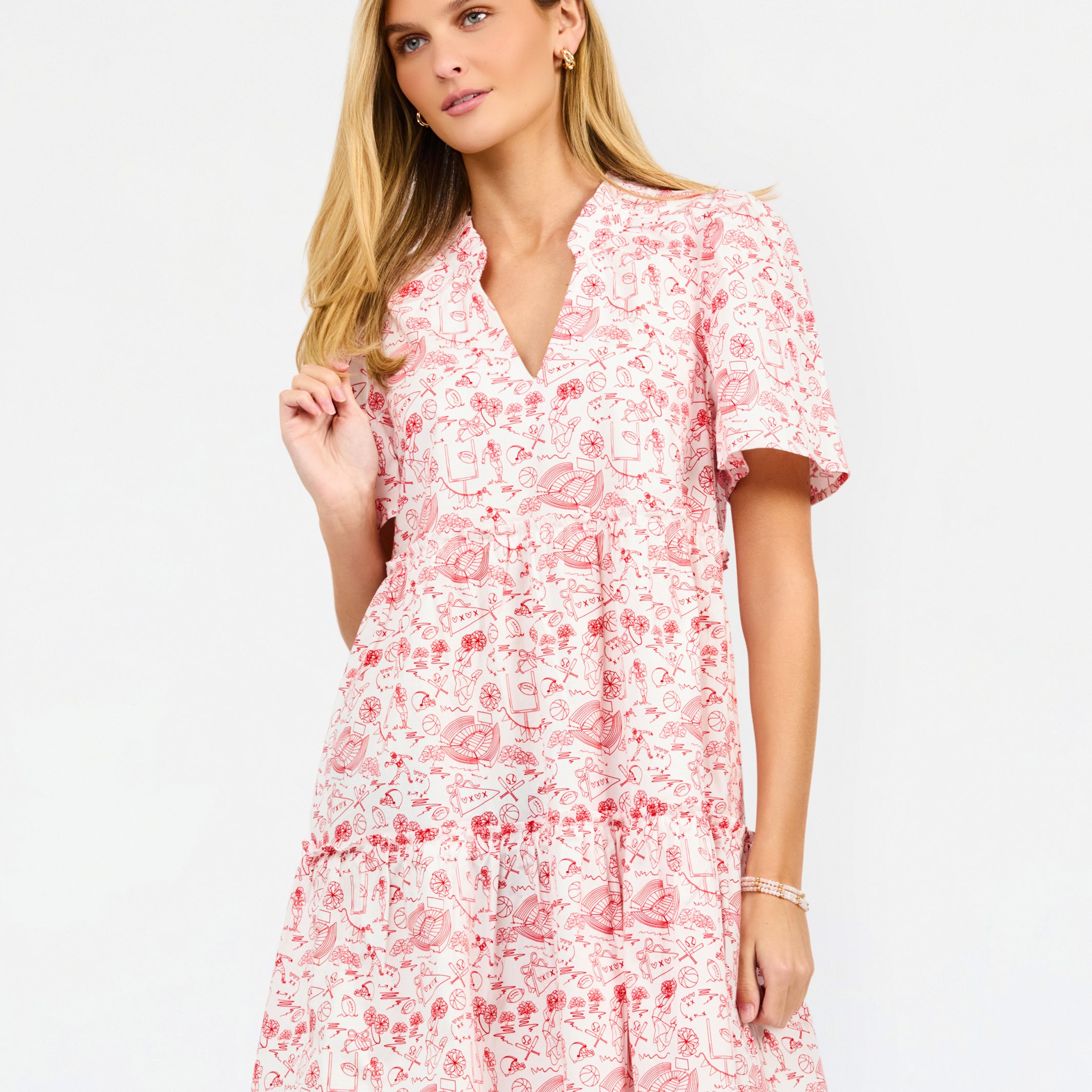 A woman modeling a short-sleeve red and white dress with a V-neckline and tiered skirt against a plain white studio background.