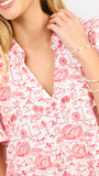 A close-up of a woman wearing a white short-sleeve dress with a red toile-style print of football game motifs. She is also wearing pearl beaded bracelets on her wrist.