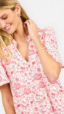 A close-up of a woman wearing a white short-sleeve dress with a red toile-style print of football game motifs. 