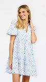 A woman modeling a short-sleeve white dress with a light blue football toile print, featuring a V-neckline and a flared skirt, set against a plain white studio background.