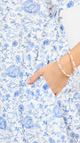 A woman modeling a short-sleeve white dress with a light blue football toile print, featuring a V-neckline and a flared skirt, set against a plain white studio background.