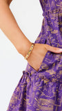 Close-up of a person wearing a purple tiered dress with a gold doodle print, showing the side pocket and hand.