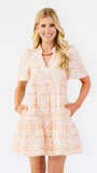 A woman modeling a short-sleeve tiered dress with a peach and white floral pattern against a plain white background.