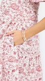 A close-up of a person wearing a white dress with a red football-themed print, featuring a pocket and a hand resting in it. The person is also wearing pearl bracelets.