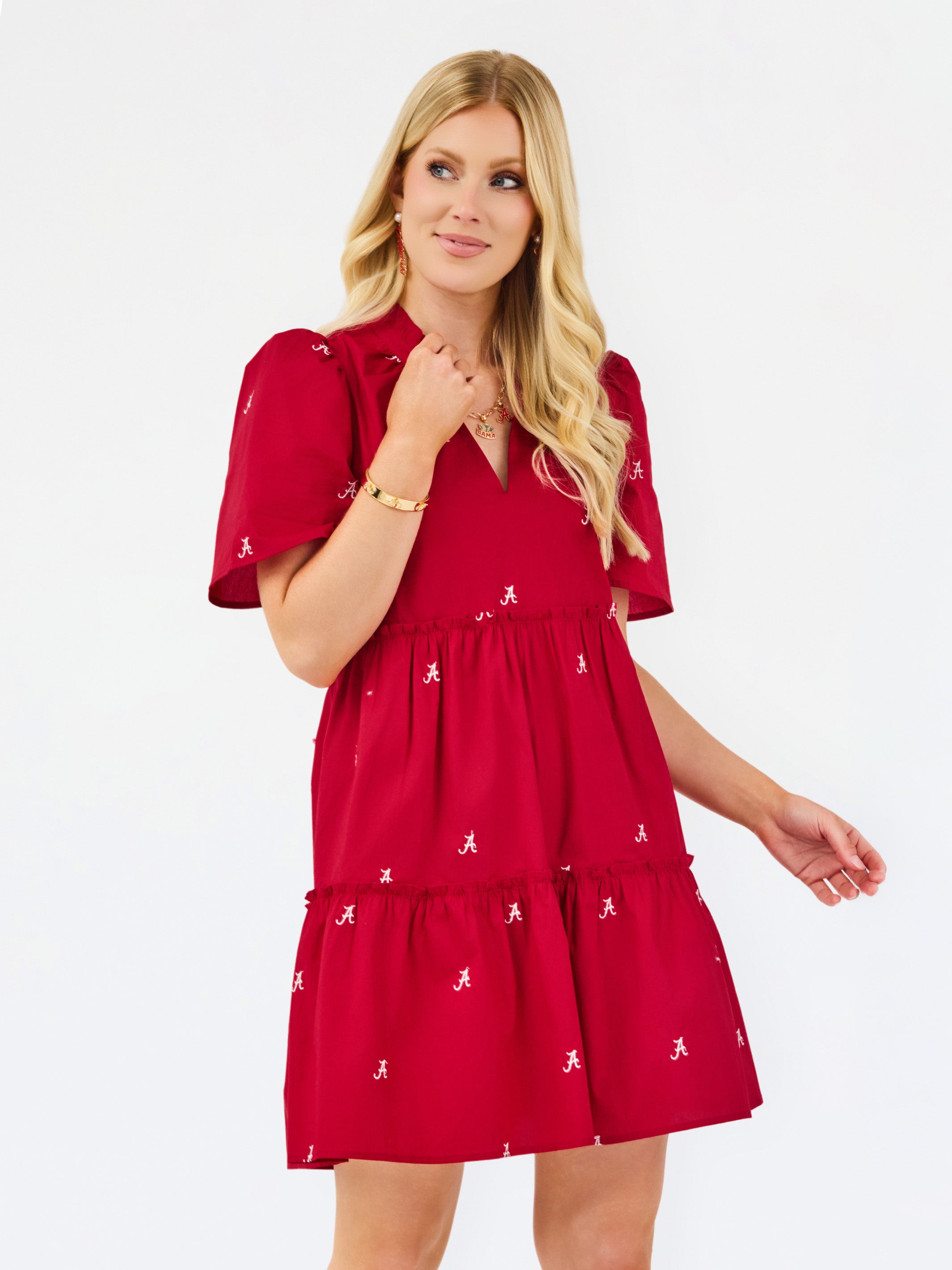 A blonde woman modeling a red tiered mini dress with short puff sleeves and small white embroidered accents, photographed against a plain white studio background.