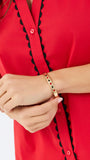 A woman modeling a bright red short-sleeve blouse with black scalloped trim along the button placket and sleeve edges, paired with white pants, against a plain white studio background.