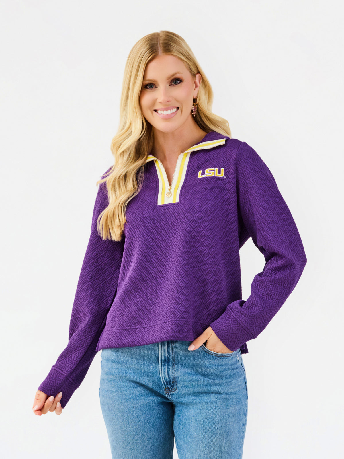 A woman wearing a purple LSU quarter-zip pullover sweater with yellow trim and blue jeans, photographed against a clean white studio background.