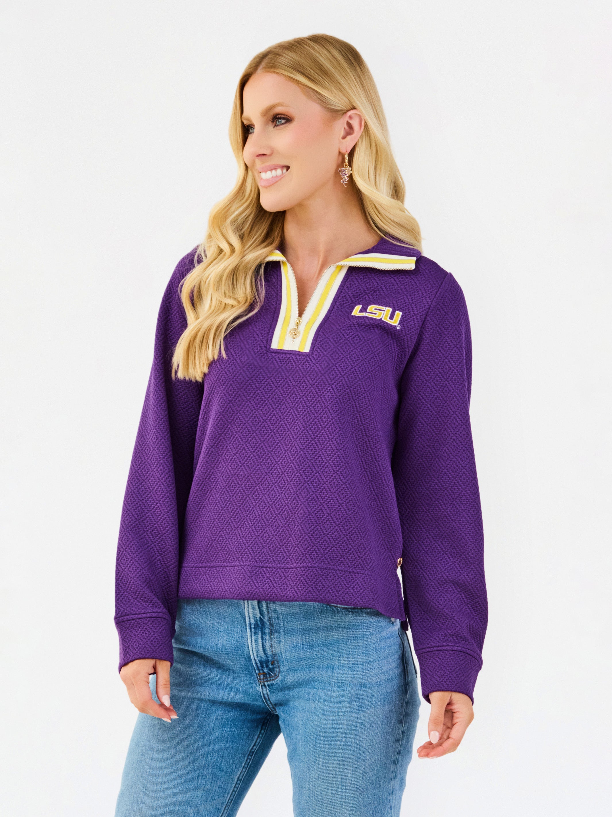 A woman wearing a purple LSU quarter-zip pullover sweatshirt with yellow and white trim, paired with blue jeans, against a plain white studio background.