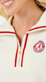 A woman modeling a cream-colored quarter-zip sweatshirt with red trim and a circular red and white logo on the left chest, paired with blue jeans against a plain white background.