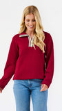 A woman wearing a burgundy long-sleeve quarter-zip sweatshirt with cream and navy striped trim on the collar, paired with blue jeans, against a plain white background.