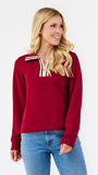 A woman wearing a long-sleeve crewneck sweater in deep burgundy with a contrasting white and burgundy striped collar, paired with blue jeans, against a plain white studio background.