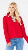 A blonde woman wearing a bright red long-sleeve knit top with a striped collar and blue jeans, standing against a plain white studio background.