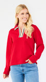A blonde woman wearing a bright red long-sleeve knit top with a striped collar and blue jeans, standing against a plain white studio background.