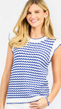 A woman modeling a sleeveless top with a blue and white wavy stripe pattern, paired with white pants, against a light gray studio background.