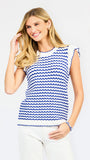 A woman modeling a sleeveless top with a blue and white wavy stripe pattern, paired with white pants, against a light gray studio background.