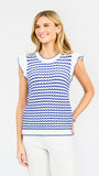 A woman modeling a sleeveless top with a blue and white wavy stripe pattern, paired with white pants, against a light gray studio background.