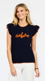 A woman modeling a navy blue ribbed knit top with orange trim and 'auburn' script across the chest, paired with white pants against a light gray studio background.