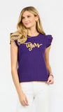 A woman modeling a purple ribbed knit top with yellow ruffle trim and 'Tigers' written across the chest in yellow script, paired with white pants against a light gray studio background.