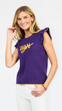 A woman modeling a purple ribbed knit top with yellow ruffle trim and 'Tigers' written across the chest in yellow script, paired with white pants against a light gray studio background.